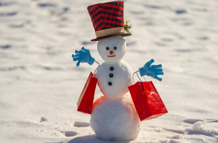 Snowman holding a Christmas gift box on winter background. Snowman with gift on a snowy winter day....