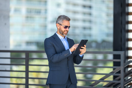 Finance expert reviewing a contract. Businessman outdoors with tablet. Businessman using tablet outside. Mature businessman checking finance data. Rich businessman reviewing contract on tablet.の写真素材