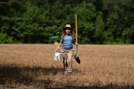 Kid holding a shovel on the farm. Child helps with farm work. Kid working in the farm field. Young...