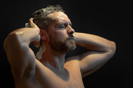 Male beauty model under a water in a shower bathroom. Mature man in shower. Latin man cleaning head under shower. Male portrait closeup with water drops on his skin in the shower.の写真素材