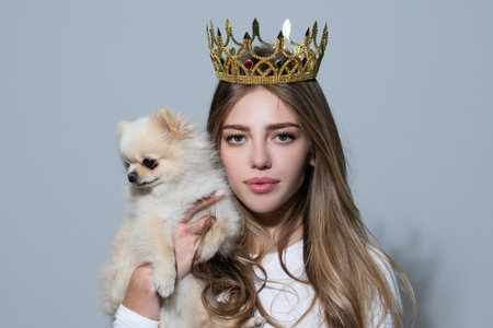 Beautiful girl dressed as a princess hold puppy. Romantic portrait with dog. Lovely girl in crown. Fairy-tale model with dogs. Woman with small dog. Cute doggy in princess hand.の写真素材