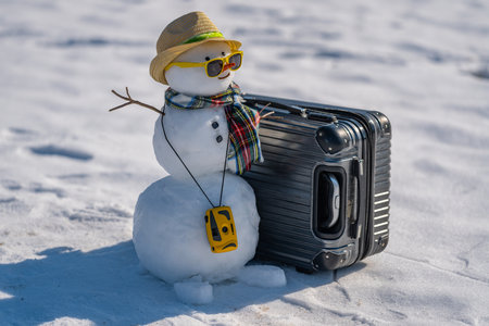 Snowman tourist with sunglasses and backpack. Funny snowman holding suitcase on snowy trip. Christmas traveler snowman with luggage. Snowman on winter vacation with camera and hat.の写真素材
