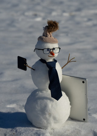 Snowman talking on smartphone in snowy landscape. Snowman making a phone call. Funny snowman using laptop outdoors. Snowman with mobile phone during winter holiday.の写真素材