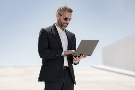 Business man using laptop outdoors. 40s man using laptop. Confident business man with laptop....