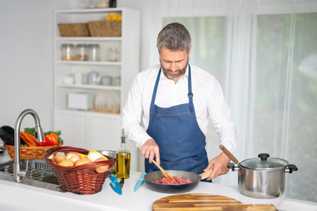 Chef chops vegetables in kitchen. Man in apron prepares healthy meal with raw ingredients. Cook with vegetables. Chef with fresh vegetables for dinner. Cook prepares breakfast with veggies.の写真素材