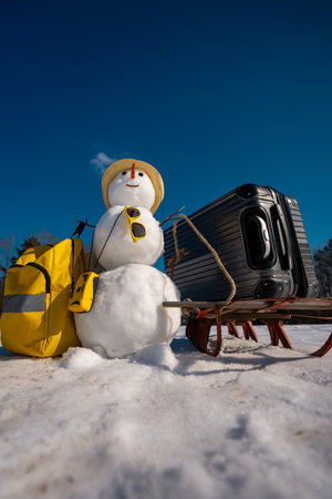 Tourist with suitcase ready for winter vacation. Snowman Tourist holding travel bag. Tourist snowman on snowy holiday adventure. Snowman tourist with backpack. Winter journey with a festive snow man.の写真素材