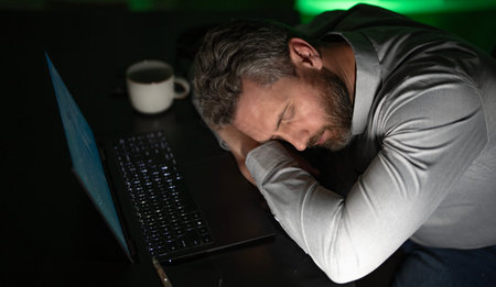 Businessman working overtime in a dark office late at night. Overworked office worker with laptop in...