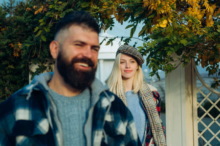 Disfocused bearded smiling man and beautiful blonde woman standing under colorful autumnal leaves....