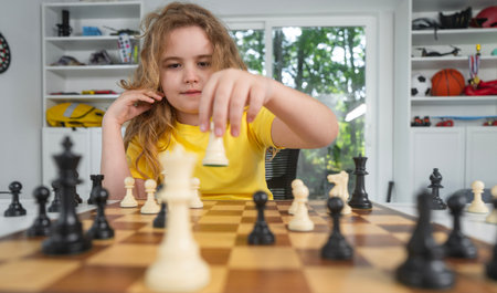 Child with chess at home. Boy studying strategy on chessboard. Cute kid playing thoughtful chess game. Schoolchild concentrating on chess figures. Teen learning logic through chess.の写真素材