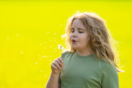 Cute blonde child face. Kid blows a dandelion. Summer kids portrait close-up. Kid with dandelions outdoors. Kid free and carefree. Dandelion seeds near child face. Kids freedom. Kids dreaming face.の写真素材