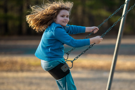 Blonde kid swinging outdoors. Laughing child on swing. Cute kid boy playing at playground. Excited kid on a swing in motion. Cute kid in summer park. Playful child swinging in park. Happy childhood.の写真素材