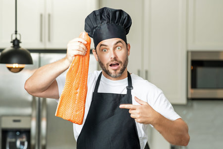 Middle aged man cooking fish salmon in kitchen. Chef on kitchen with fish salmon. Health, natural...