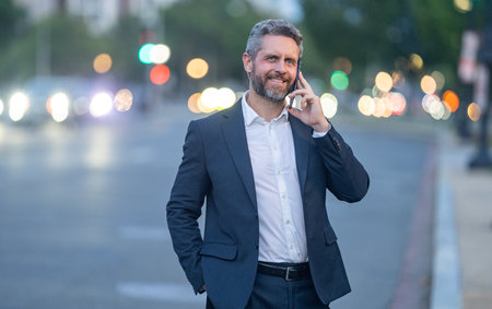 Business talk. Businessman talking on smartphone while walking in the city at night. Business late call. Business conversation overtime work. Business man man in a suit speaking on the phone outdoor.の写真素材