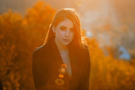 Autumn woman walking through park. Romantic portrait with falling maple leaves. Chic girl posing in...