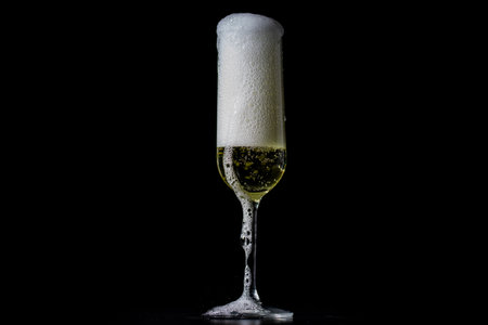 Champagne sparkling in a crystal glass. Pouring bubbly champagne with festive bubbles. Close-up of sparkling wine splash in elegant wineglass. Champagne drink with golden fizz on black background.の写真素材