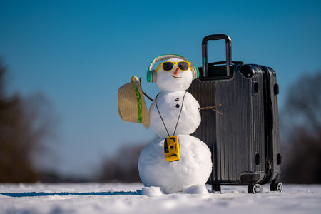 Snowman traveler with suitcase and headphones. Winter music. Funny snowman listening to music. Snowman with earphones. Winter music. Snowman celebrating with music and travel gear. Christmas songs.の写真素材