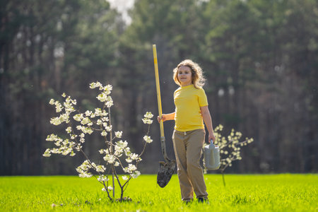 Little helper in the backyard garden. Kid planting trees. Outdoor gardening for children. Kid watering a young plant. Childhood development. Farm life with kids planting trees. Orchard filled.の写真素材