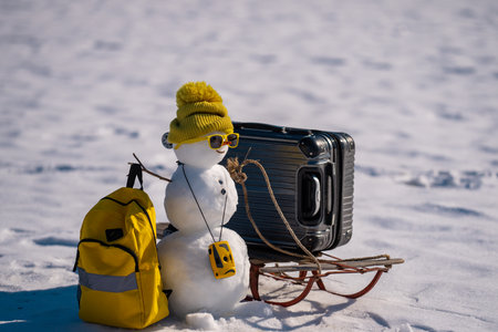 Snowman with suitcase ready for holiday trip. Winter vacation starts with snowman. Christmas snowman holding travel bag outdoors. Festive snowman tourist on snowy adventure. New Year journey.の写真素材