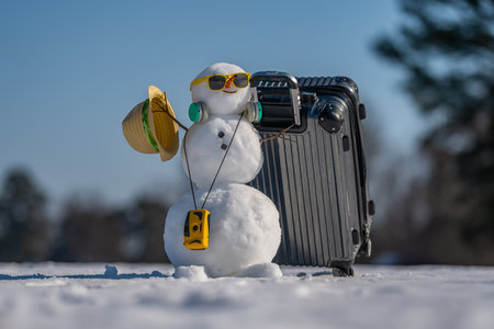 Snowman tourist with sunglasses and backpack. Funny snowman holding suitcase on snowy trip. Christmas traveler snowman with luggage. Snowman on winter vacation with camera and hat.の写真素材