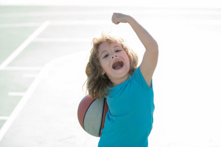 Child playing basketball on outdoor court. Happy child boy hold basketball ball. Summer sport kids. Kid on basketball game. Sporty kid training basketball on playground. Outdoor activity for children.の写真素材