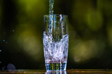 Pouring clean water in glass on green nature background. Fresh water pour.
