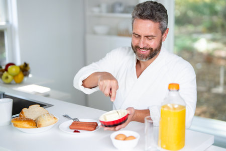 Happy man eating morning breakfast. Healthy food in kitchen for aged mature man. Portrait of senior man at kitchen and eat lunch. 50s man eating breakfast in cozy kitchen at home.の写真素材