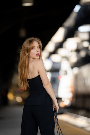 Stylish woman waiting for a train at the station. Beautiful girl on travel adventure. Fashionable tourist near railway platform. Young traveler enjoying her urban journey. Model on vacation trip.の写真素材