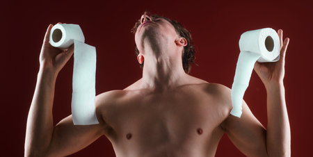 A man holds toilet paper like a restroom emergency. Funny restroom concept with dramatic expression. Restroom panic shown with tissue rolls. A man holds toilet paper rolls in a dramatic pose.の写真素材