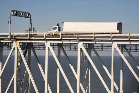 Cargo truck travels on bridge. Steel beams support highway. Logistics route over water. Industrial transport moves freight. Infrastructure enables shipping.の写真素材