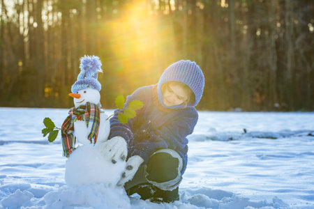 New Year holiday. Child playing with snowman in snow field. Kids winter activity. Kids winter creativity in snowy field. Kid building snowman. Kids winter fun. Kids winter holiday in snowy field.の写真素材