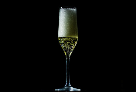 Sparkling wine splash in elegant wineglass. Champagne drink with golden fizz on black background.の写真素材