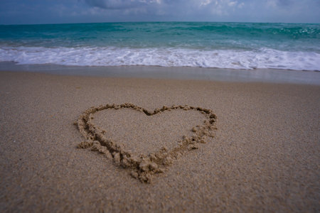 Heart drawn in sand. Waves forming a heart shape sign. Love on beach. Romantic summer. Heart made of sand. Love and ocean waves.の写真素材