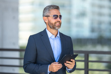 Urban entrepreneur reviewing business strategy. Businessman outdoors on tablet. Business man using tablet outside. Business man checking finance data. Rich business man reviewing contract on tablet.の写真素材