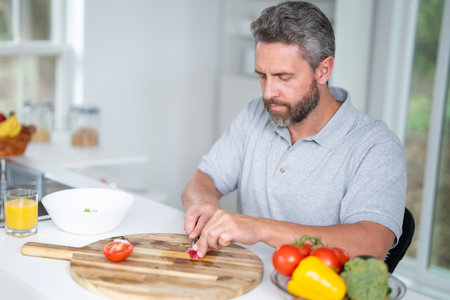 Mature Man eat breakfast in the kitchen on a morning. Guy eat vegetables for a healthy meal in his kitchen in the morning. Cozy kitchen. Morning breakfast in the white kitchen.の写真素材