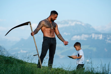 Father and his son work together on grass farm. The father teaches his child. Father and child on grass farm. The dad shows his son tablet. Son helps his father.の写真素材