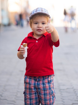 A cute baby enjoys eating ice cream outdoors. Sweet treat brings joy and happiness. Little kid tastes ice cream. Happy childhood. Summer kids snack. Baby smiles with ice cream.の写真素材