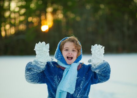 Child during snowball fight outdoors. Winter happiness. Kid playing snowball fight in forest sunlight. Playful child throwing snowball on winter nature.の写真素材
