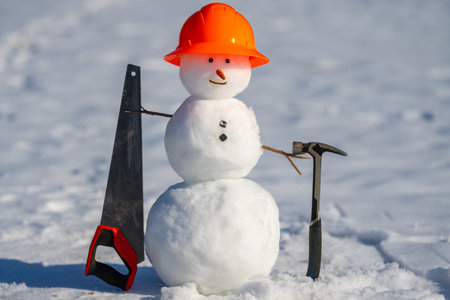 Creative snowman worker with construction tools and hardhat. Cute snow man builder. Snowman engineer holds hammer and measures. Snowman handyman using tools. Builder snowman ready for repair work.の写真素材