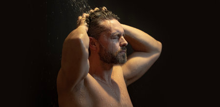 40s man taking a shower and washing his face with soap. Mature male in the bath. Guy applying shampoo and foam to his hair in the bathroom. Man washing body and face in a modern bathtub.の写真素材