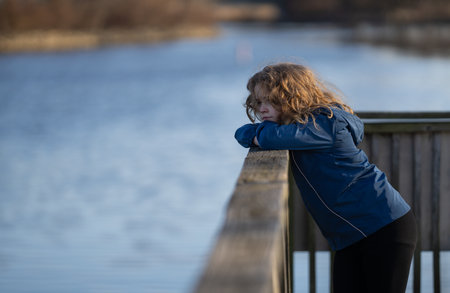 Kid on a pier near the river. Kid walk on rocks by the river. Child thoughtful outdoors. Calm and quiet time near the river. Peaceful childhood. Child on fresh air in autumn fall park.の写真素材