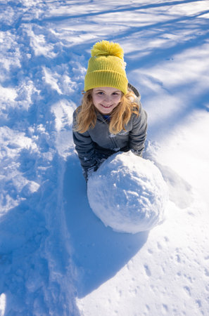 Happy winter. Kid having fun outdoors with snowball. Kid playing in fresh snow under blue sky. Playful child enjoying sunny winter day in nature.の写真素材
