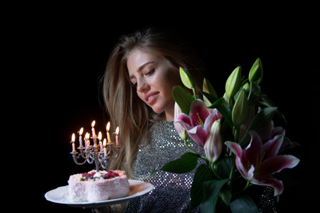 Dreamy girl celebrating birthday with flowers and cake. Model celebration birthday. Beautiful lady holding bouquet and festive dessert. Romantic birthday. Girl with pink lilies and birthday cake.の写真素材