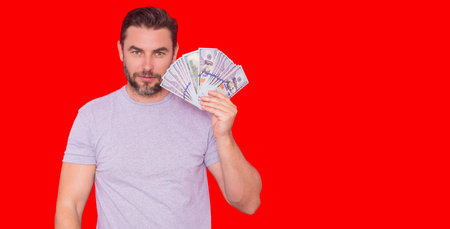 Good payment. Handsome man holding money isolated over red studio, banner copy space. Money in...