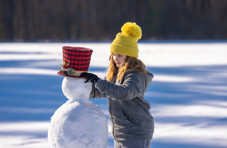 Kid building a snowman on winter day. Childhood and winter fun. Kid creating snowman outdoors. Kid...