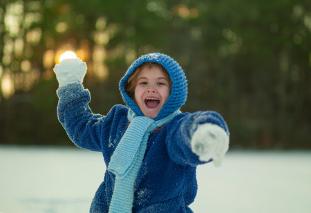 Happy kid enjoying outdoor snowball battle. Cute throwing snow outdoors. Winter day with child throwing snowballs. Child enjoying winter snowball play.の写真素材