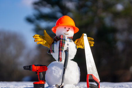 Snowman handyman holding saw and hammer. Snow man carpenter. Snowman worker with hardware. Snowman construction DIY in winter.の写真素材