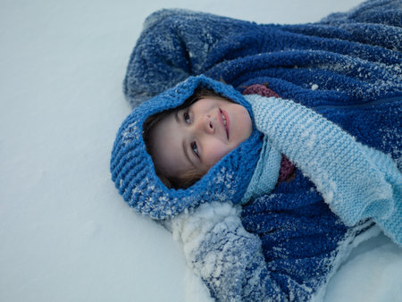 Winter kids happiness. Cute excited boy in winterwear lying in snow. Winter Vacation. Winter journey with kids. Child playing in snowy winter day. Happy kid enjoying snow falling.の写真素材