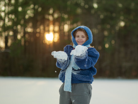 Playful kid making and throwing snowballs. Child during snowball fight outdoors. Winter happiness. Kid playing snowball fight in forest sunlight. Playful child throwing snowball on winter nature.の写真素材