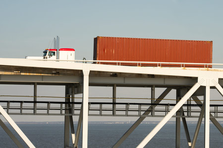 Container truck travels roadway. Freight moves across bridge. Logistics support global trade....