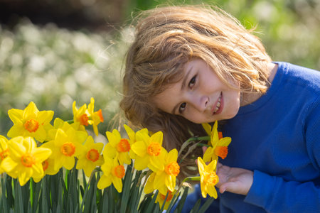 Spring fun for kids. Child play outdoors in a beautiful spring garden. Kid face in flowers. Adorable...